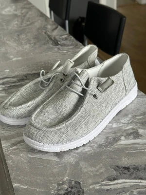 Ljusgrå loafers med vit sula - Snygga ljusgrå loafers i textil med vit, tjock sula och minimalistisk design. Skorna har dekorativa snören framtill och en stilren, modern look som passar till många outfits. Perfekta för dig som gillar en clean och avslappnad stil. Endast provade 