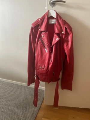 Röd skinnjacka från Stand - Snygg röd skinnjacka från Stand med klassisk bikerstil, silvriga dragkedjor och nitar. Jackan är gjord av det mjukaste skinnet, axelklaffar och bälte i midjan för extra edge. Perfekt för vår sommarjacka. Pris på Vestiare är ca 3000kr. 