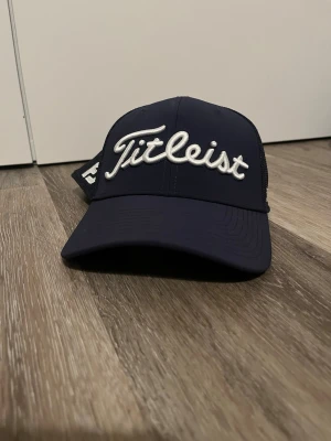 Mörkblå Titleist keps mesh Pro V1 - Snygg mörkblå keps från Titleist med broderad logga framtill och texten Pro V1 på sidan. Kepsen har böjd skärm och mesh-paneler bak för extra ventilation. Perfekt för golfbanan eller en sportig look. Pris kan absolut diskuteras.   