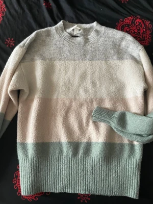 Randig stickad tröja från H&M - Mysig stickad tröja från H&M med breda blockränder i ljusgrått, beige och mintgrönt. Tröjan har rund halsringning, ribbade muddar och nederkant. 
