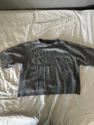 Grå stickad tröja med rund hals - En enkel och stilren grå stickad tröja med rund hals och korta ärmar. Tröjan har en normal passform och ribbstickade detaljer vid hals, ärmslut och nederkant. Perfekt för lager-på-lager och chill dagar.