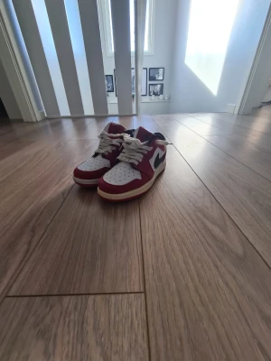 Nike Air Jordan 1 Low röd/vit - Snygga Nike Air Jordan 1 Low sneakers med klassisk röd och vit färgkombination, svart swoosh och vita skosnören. Skorna har perforerad tåbox och låg profil som ger en cool och sportig look. Perfekta för dig som vill sticka ut med stil.