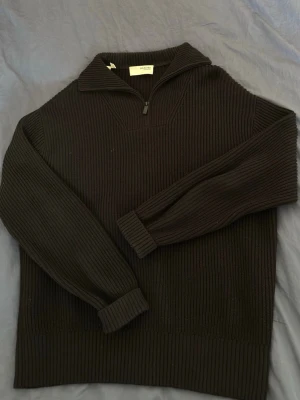 Stickad tröja - Svart stickad tröja från Selected Homme med ribbad struktur och halv dragkedja vid kragen. Tröjan har lång ärm och breda muddar vid ärmslut och nederkant. Perfekt för lager-på-lager och en stilren look.