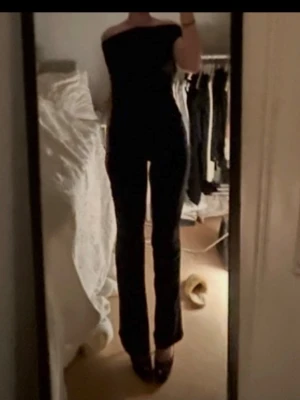 Svart off-shoulder jumpsuit - En svart, stilren jumpsuit med off-shoulder design och långa, raka ben. Snygg och figurnära passform som framhäver siluetten. Perfekt för dig som vill ha en enkel men trendig look. Materialet ser ut att vara stretchigt och bekvämt.