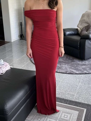 Röd offshoulder långklänning - Snygg röd långklänning med offshoulder-design och slits på sidan. Klänningen har en tight passform som framhäver figuren och är perfekt för dig som vill sticka ut. Materialet är mjukt och följsamt, vilket gör den bekväm att bära hela kvällen. Sliten är skräddar sydd!! Därav dyrare pris 
