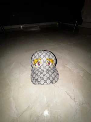  keps med tigertryck - Snygg keps med klassiskt GG-mönster och två färgglada tigerhuvuden framtill. Kepsen har svart mesh på baksidan för extra ventilation och justerbar passform. Perfekt för dig som vill sticka ut med en lyxig accessoar.