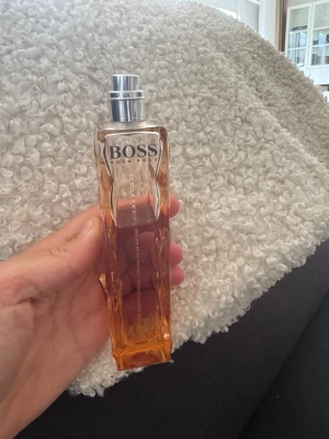 Hugo Boss Orange EdT parfym - Säljer en Hugo Boss Orange EdT parfym i en snygg, fyrkantig glasflaska med vågigt mönster. Flaskan är transparent med en varm orange ton och har en silverfärgad spraykork. Perfekt för dig som gillar fräscha och energiska dofter.