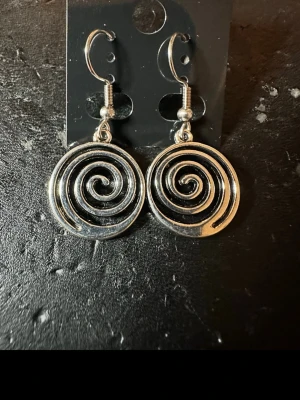 Silvriga spiralörhängen  - Säljer ett par coola silvriga örhängen  med spiralformad design. De är tillverkade i metall och har en unik, snurrad look som verkligen sticker ut. Perfekta för dig som gillar att addera lite edge till din stil.