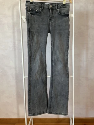 Grå jeans från Grunt - Säljer ett par grå bootcut jeans från Grunt med klassisk femficksmodell och knappgylf. Jeansen har en tvättad look och är tillverkade i ett mjukt denimtyg som passar perfekt till en avslappnad stil. 