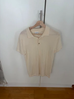 Beige polotopp från John Henric - Säljer en stilren beige polotopp från John Henric  med klassisk krage och korta ärmar. Toppen har knappar framtill och är gjord i mjukt bomullsmaterial. Perfekt för dig som gillar en enkel och clean look.
