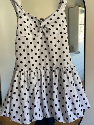 Vit prickig kort klänning - Söt vit klänning med svarta prickar och breda axelband. Klänningen har en volangig kjol och en liten knutdetalj framtill vid bysten. Köpte klänningen på Plick flr 1000kr men den var tyvärr för stor för mig. 