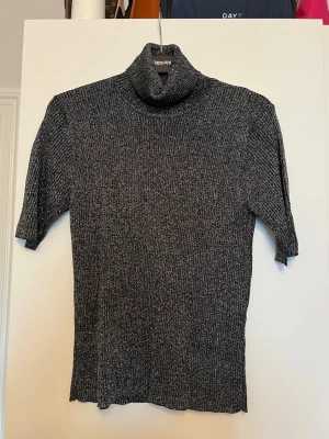 Glittrig svart polotröja från KappAhl - Säljer en svart stickad polotröja från Olsen med glittriga inslag. Tröjan har ribbad struktur, halvlånga ärmar och hög polokrage. Materialet är mjukt och stretchigt med metallictråd som ger en snygg glansig effekt. Står ingen storlek men hade gissat på XS. 