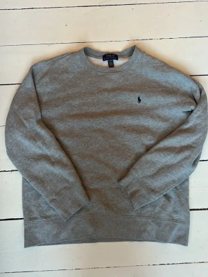 Grå sweatshirt från Polo Ralph Lauren - Säljer en klassisk grå sweatshirt från Polo Ralph Lauren med rund hals och diskret broderad logga på bröstet..Perfekt för en avslappnad och stilren look. Storleken är L(14-16år) vilket motsvarar ungefär xs. Den är använd men inga större defekter. Hör av er vid frågor!