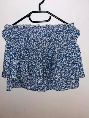 Blå blommig kortkjol med volang - Blå kjol med vita blommor på, har byxor under kjolen. Använt 1 gång och är i jätte bra skick. Skriv om du har frågor.