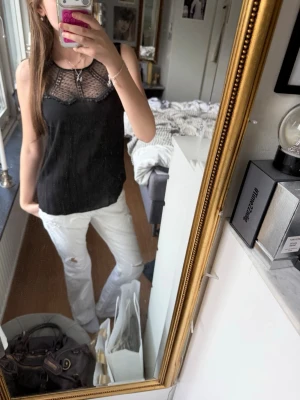 Svart spetsdetaljerad linnetopp💖 - Snygg svart linnetopp med transparent spets upptill och ärmlös design. Toppen har rund halsringning. Perfekt att styla med jeans eller kjol för en trendig look!!!