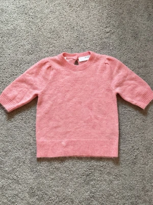 Rosa stickad tröja XS - Söt rosa stickad tröja i storlek XS med rund halsringning och ribbade muddar. Tröjan har lätt puffade axlar och är tillverkad i ett mjukt, fluffigt material som känns riktigt mysigt. Perfekt för dig som gillar en feminin och enkel stil.