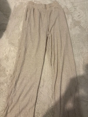 Beige ribbade mjukisbyxor XS - Säljer ett par helt oanvända beige ribbade mjukisbyxor i storlek XS. Byxorna har resår i midjan och är tillverkade i ett mjukt, stretchigt material. Perfekta för chill dagar hemma eller när du vill vara extra bekväm.