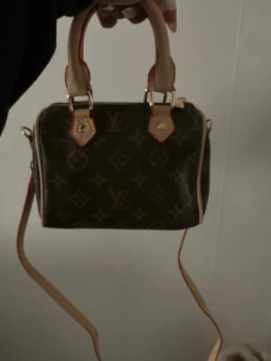  monogram handväska - Snygg handväska i klassiskt brunt monogrammönster med ljusa läderdetaljer och guldfärgade metalldelar. Väskan har både handtag och en avtagbar axelrem, perfekt för dig som gillar ikoniska accessoarer.