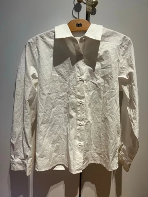 Vit klassisk skjorta  - Vit skjorta med klassisk krage och knappar framtill Skjortan har långärmade ärmar och är tillverkad i bomull, vilket gör den bekväm och enkel att styla. Perfekt för dig som gillar en clean och tidlös look.