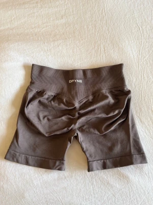 Dfyne shorts - Dfyne gym-shorts i impact modellen, bruna med buttscrunch, låg midja och väldigt strechiga. Köpta i storlek S men passar även XS då de är små i storleken