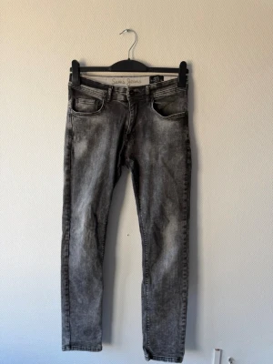  Sams Jeans - Säljer ett par grå slim fit jeans från Sam's Jeans med klassisk femficksdesign och snyggt tvättad look. Jeansen har knapp- och dragkedjeförslutning samt bälteshällor. Perfekta för dig som gillar en modern och avslappnad stil.