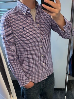 Rutig skjorta från Ralph Lauren - Klassisk rutig skjorta från Ralph Lauren i blått, rött och vitt. Skjortan har lång ärm, knappar framtill och en liten broderad logga på bröstet. Tillverkad i bomull och har en normal passform. Perfekt för en clean och stilren look.