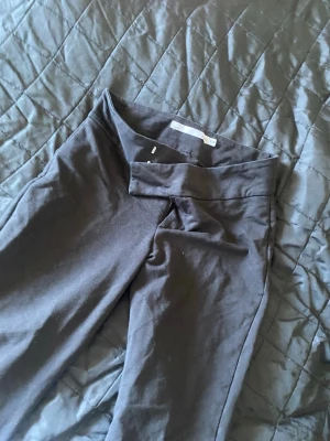 Svarta leggings med crossover-midja - Säljer ett par svarta byxor med snygg crossover-detalj i midjan. De är tighta och har en hög midja som ger en cool och modern look. Materialet är stretchigt och bekvämt, perfekt för att matcha med oversized tröjor eller crop tops.