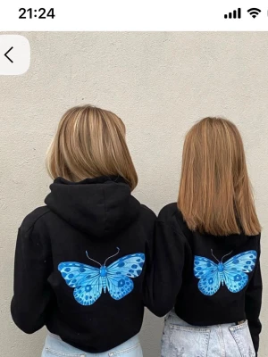 THE COOL ELEPHANT HOODIE - Cool svart hoodie från The Cool Elephant med en stor blå fjäril på ryggen och en mindre fjäril på bröstet. Hoodien har huva med snören och är tillverkad i mjukt material som passar perfekt för en avslappnad look.