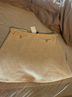 Beige stickad kortkjol med knappar - Säljer en beige stickad kortkjol med två dekorativa knappar framtill. Kjolen har en enkel och stilren design med lätt struktur i materialet. Perfekt för dig som gillar en clean och modern look.