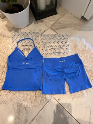 Electric blue DFYNE - Säljer ett blått träningsset från DFYNE med en sportig topp med smala axelband och matchande shorts. Setet är tillverkat i ett stretchigt och funktionellt material som passar perfekt för gym och träning. Logotypen är tryckt på både topp och shorts. Modell: impact 4.5