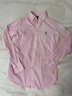 Ralph Lauren skjorta rosa - Rikigt härlig färg på denna underbara Ralph Lauren skjortan! Perfekt nu till sommaren och Valborg! Inga defekter förutom en liten fläck på baksidan och att den har krymt i tvätten! Skriv om ni har funderingar eller frågor✅