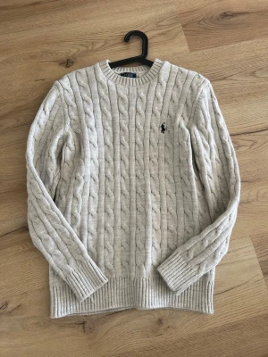 Beige stickad tröja Polo Ralph Lauren - stickad tröja i beige från Polo Ralph Lauren med rund halsringning och ribbade muddar. Tröjan har det klassiska broderade logotypen på bröstet och är tillverkad i ett mjukt material som passar perfekt till alla årstider, pris kan är diskuterbart !😆🫱🏻‍🫲🏼