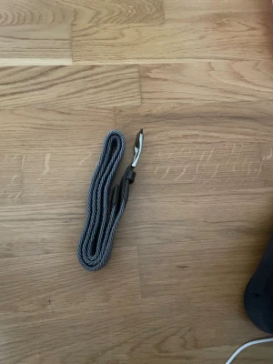 Grått flätat bälte med silverdetaljer - Snyggt grått flätat bälte med silverfärgat spänne och svarta skinnliknande detaljer vid ändarna. Perfekt för att ge din outfit en clean och stilren touch. Passar till både jeans och chinos. Aldrig använt på grund av att jag glömt att jag har det
