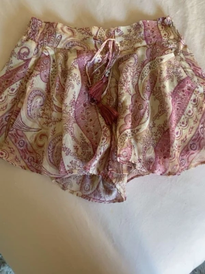 Mönstrade shorts med snörning ifrån hm💓💓 - jag säljer ett par shorts som liknar en kjol också, den har ett mönster med beigea och rosa nyanser. Shortsen har en låg midja med snöre där fram och tofsar på snörena. De är ifrån hm i storlek xs💓💓de är aldrig använda men prislappen är borttagen