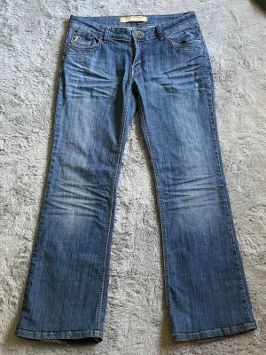 Lågmidjade bootcut jeans från Dromedar - Snygga blå bootcut jeans från Dromedar med klassiska kontrastsömmar och fem fickor. Jeansen har en låg midja och detaljerade bakfickor med broderi. Perfekta för dig som gillar y2k stilen. Alla bud på 250kr & över accepteras!         Midjemått: 42cm Grenmått: 21cm Innerbenslängd: 77cm Totallängd: 103cm 