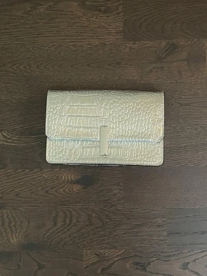 Silverfärgad kuvertväska i croco-mönster - Snygg kuvertväska i metallic silver med croco-mönstrad yta. Väskan har en stilren, rektangulär form och stängs med ett lock framtill. Perfekt accessoar för att lyfta din outfit med en trendig touch. (Tillkommer axelrem)🩷skriv vid frågor!