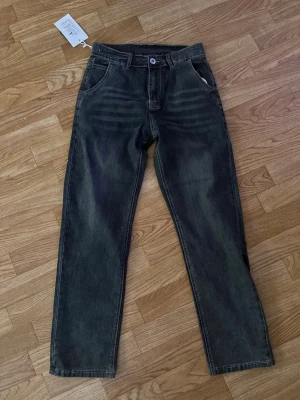Svarta raka jeans med prislapp kvar  - Säljer ett par svarta raka jeans med klassisk femficksmodell och läderpatch bak i midjan. Jeansen har en avslappnad passform och är tillverkade i slitstark. Perfekta för en cool och enkel stil. NYPRIS 500kr