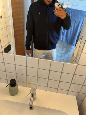 Marinblå hoodie från Polo Ralph Lauren - Säljer en marinblå hoodie från Polo Ralph Lauren med klassisk broderad logga på bröstet. Tröjan har huva med snörning, dragkedja framtill och två fickor. Perfekt för dig som gillar stilren och sportig look. Har inget kvitto på den.