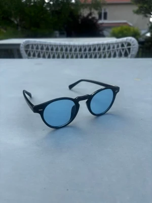 Svarta solglasögon med blåa glas - Snygga solglasögon med rundad svart båge och ljusblått glas. Onesize. Knappast använda.