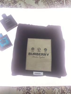 Svart sweatshirt från Burberry - Svart sweatshirt från Burberry med beige rektangulär patch och logga på bröstet. Klassisk rund halsringning och ribbade muddar. Perfekt för dig som gillar stilrena och exklusiva plagg med tydlig branding.