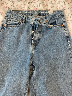 Blå wide leg jeans regular fit - För dej som gillar bagijeans! Säljer ett par ljusblå jeans med wide leg och regular fit. Klassisk femficksmodell med hög midja och raka, vida ben. Jeansen har knappgylf och är tillverkade i kraftig denim. Perfekta för en avslappnad och trendig look.