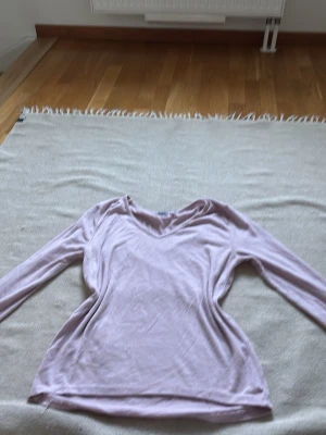 Ljuslila långärmad topp - En enkel och mjuk långärmad topp i ljuslila färg. Toppen har v-ringad hals och är tillverkad i ett tunt, stretchigt material som känns skönt mot huden. Perfekt att styla med jeans eller kjol för en avslappnad look.