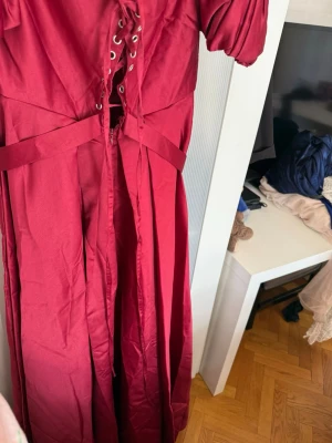 Vinröd långklänning med snörning - Säljer en vinröd långklänning med puffärmar och snygg snörning framtill. Klänningen har offshoulder-modell och ett markerat midjeband som ger en fin siluett. Perfekt för dig som vill sticka ut med en unik och elegant look.