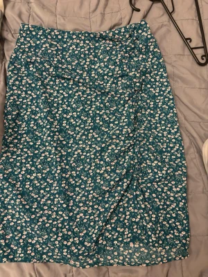 Blommig blå kjol från SHEIN - Supersöt blå kjol från SHEIN med små vita och rosa blommor över hela tyget. Kjolen har en rak passform och är i ett lätt material som passar perfekt till varmare dagar. Enkel att matcha med både t-shirt och linne.