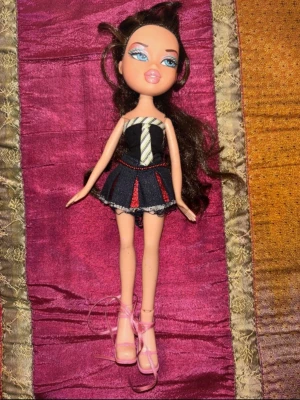Vintage Bratz – Y2K – tidigt 2000-tal - Original Bratz-docka från tidigt 2000-tal.  Dockan har klassisk Y2K-look med kort jeanskjol, topp med slipsdetalj och rosa klackskor enligt bilder. Hår, ansikte och kropp i mycket fint begagnat skick med normalt slitage för åldern.  Perfekt för samlare eller dig som gillar tidiga Bratz.  Skick: mycket bra Märke: Bratz (MGA) Era: ca 2002–2004