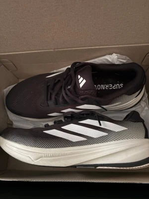 Adidas Supernova svartvita sneakers - Snygga Adidas Supernova sneakers i svart och vitt med klassiska tre ränder på sidan. Ovandelen är i mesh för bra andningsförmåga och sulan har Dreamstrike-dämpning för extra komfort. Perfekta för dig som gillar sportig stil och vill ha sköna springskor.