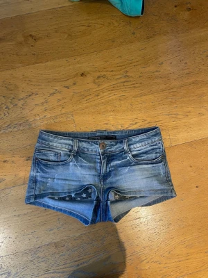 Blå denimshorts från Only - Säljer ett par blå denimshorts från Only med låg midja och klassisk femficksdesign. Shortsen har slitna detaljer och stjärnmönster på insidan av fickorna. Perfekta för sommarens alla äventyr!