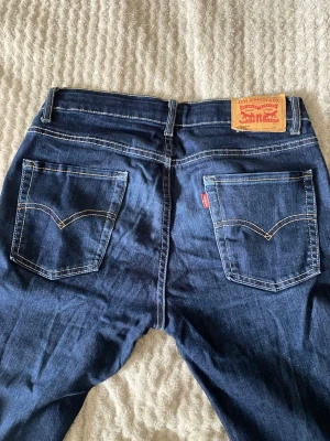 Levi's 510 mörkblå jeans - Säljer ett par mörkblå Levi's 510 jeans med klassiska bakfickor och kontrastsömmar. Jeansen har en slim fit-modell och är tillverkade i ett mjukt denimtyg. Perfekta för dig som gillar en tidlös och clean look.
