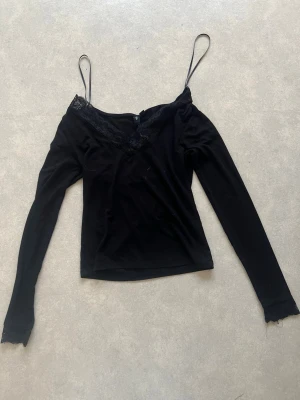 Svart långärmad topp med spets - Snygg svart långärmad topp v-ringad spetskant framtill. Toppen har en croppad passform och är tillverkad i mjukt material som känns skönt mot huden. Perfekt för dig som gillar en trendig och stilren look.