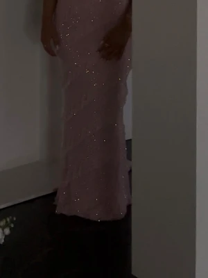 Lila glittrig långklänning med volang - Säljer en lila långklänning med glittrigt tyg och volangdetaljer. Klänningen har en figurnära passform och är perfekt för dig som vill sticka ut. Materialet är glittrigt och skimrar snyggt i ljuset.